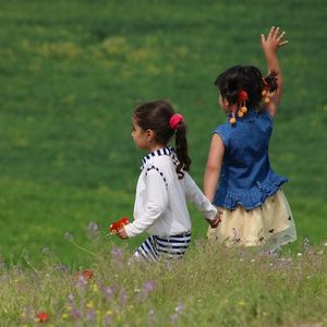 Photo Credit: Firoz Sidiqy. Young sisters holding hands in a green field facing away with one girl waving to someone off frame.